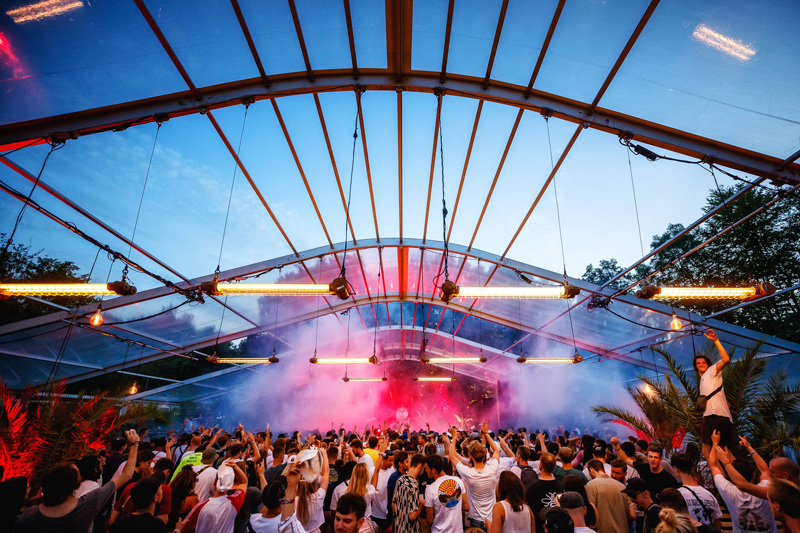 Foule dans un festival en plein air sous une structure transparente avec lumières colorées et fumée