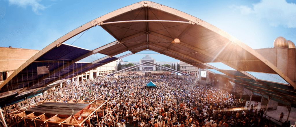 Foule dans un festival en plein air sous une structure transparente avec lumières colorées et fumée